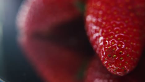 macro epic video of a pile of strawberries, red strawberry, green leaf, tiny seeds, on a rotating reflection stand, smooth movement