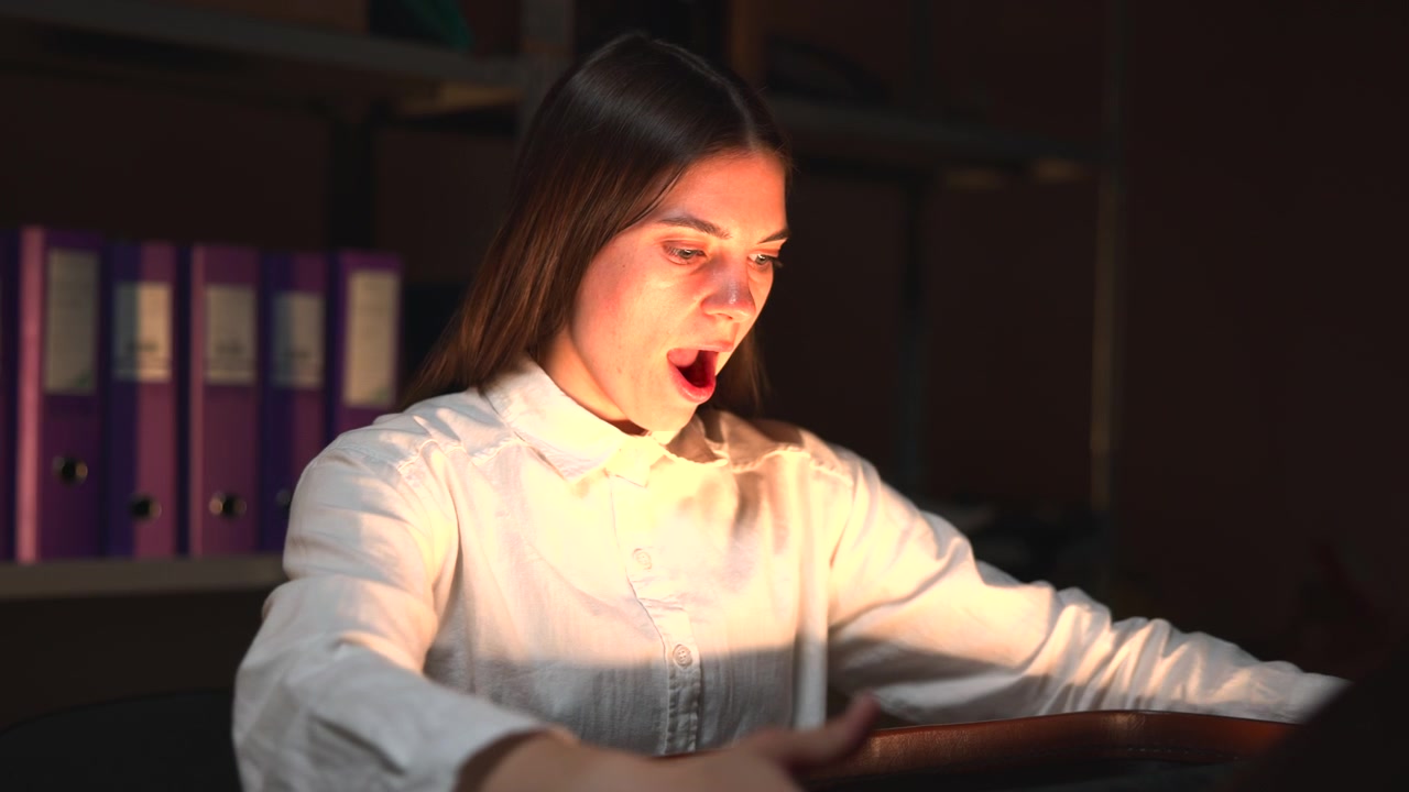 Primo piano di una valigia scura chiusa appoggiata su una superficie chiara, con una chiusura metallica visibile, bordo arrotondato, finitura lucida e sfondo sfocato in un ambiente interno poco illuminato.