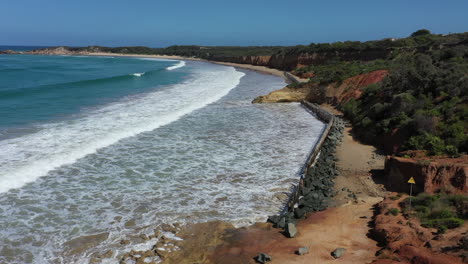 Aerial:-Rip-Rap-fence-prevents-erosion-at-Soapy-Rocks-Beach,-Anglesea