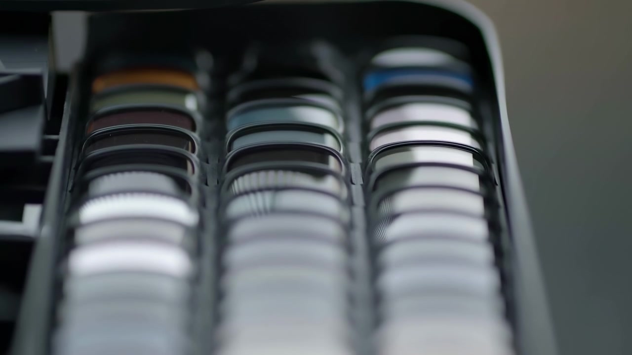 Close-up view of optics case in gradual opening pose, showing multiple stacked circular lenses arranged in molded tray, with soft diffused light, glossy surfaces, precise product order