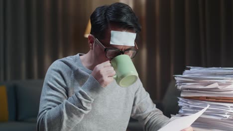 close up of sick asian man drinking water while working hard with documents at the home