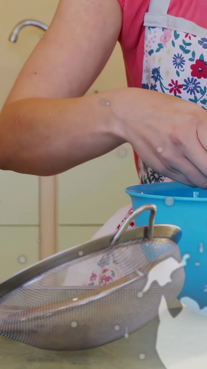 Video verticale: Un cuoco casalingo posiziona un setaccio, poi solleva una ciotola blu e versa il latte, preparando l'impasto.