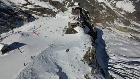 Vista-Aérea-De-Una-Pista-De-Esquí-Con-Entusiastas-De-La-Montaña-En-Saas-Fee,-Estación-De-Los-Alpes-Suizos