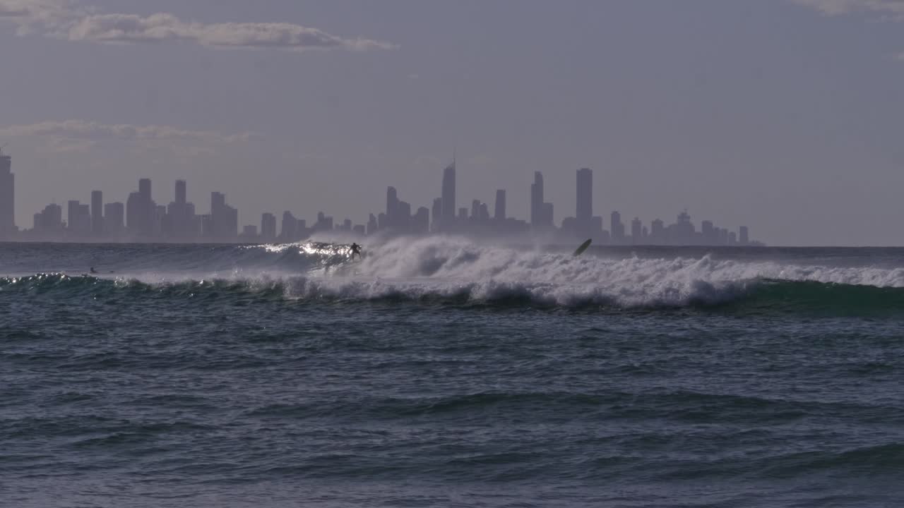 Powerful Ocean Waves With Adventurous Surfers At Currumbin Alley Beach. Surfers Paradise Cityscape In Background. wide shot