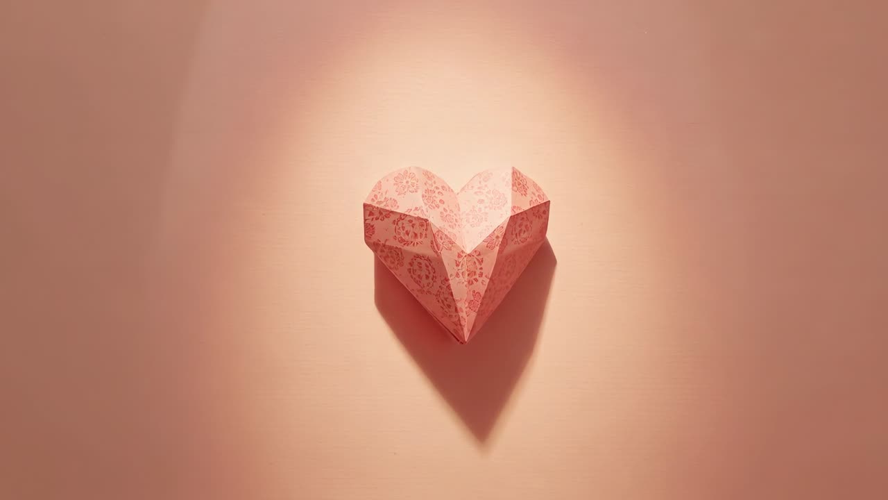 Shifting camera revealing origami heart on pink wall in studio, spotlight showing right facet