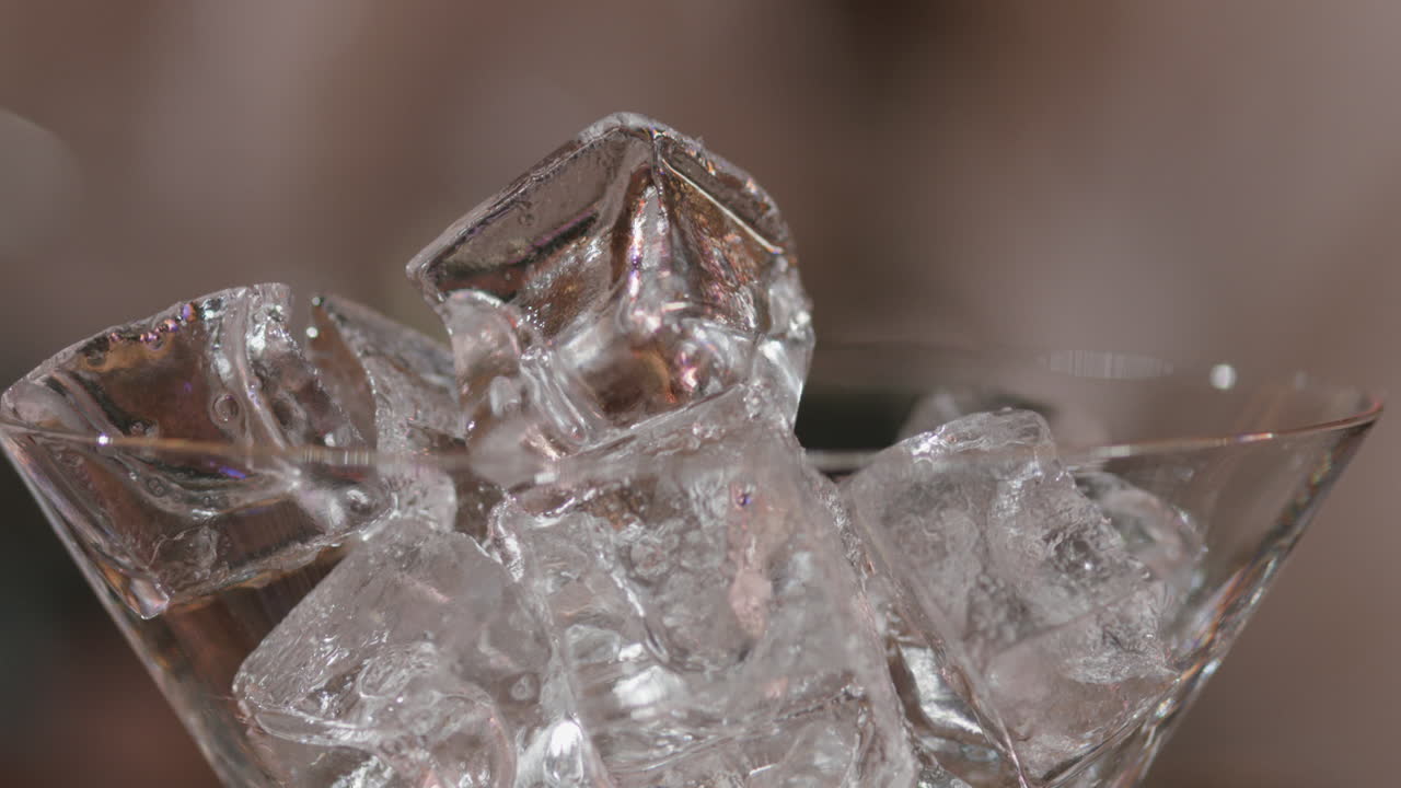 Detailed close-up of a martini glass filled with ice cubes next to a glass of whiskey, ideal for representing the art of mixology, premium drinks.