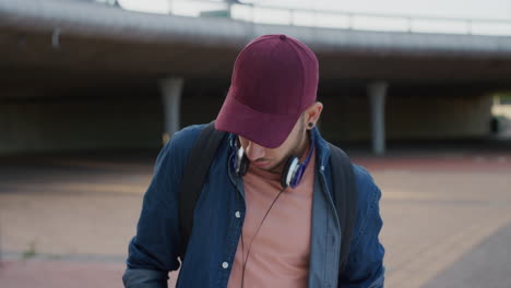 retrato de un joven estudiante hispano que usa un teléfono inteligente esperando en una ciudad urbana con sombrero