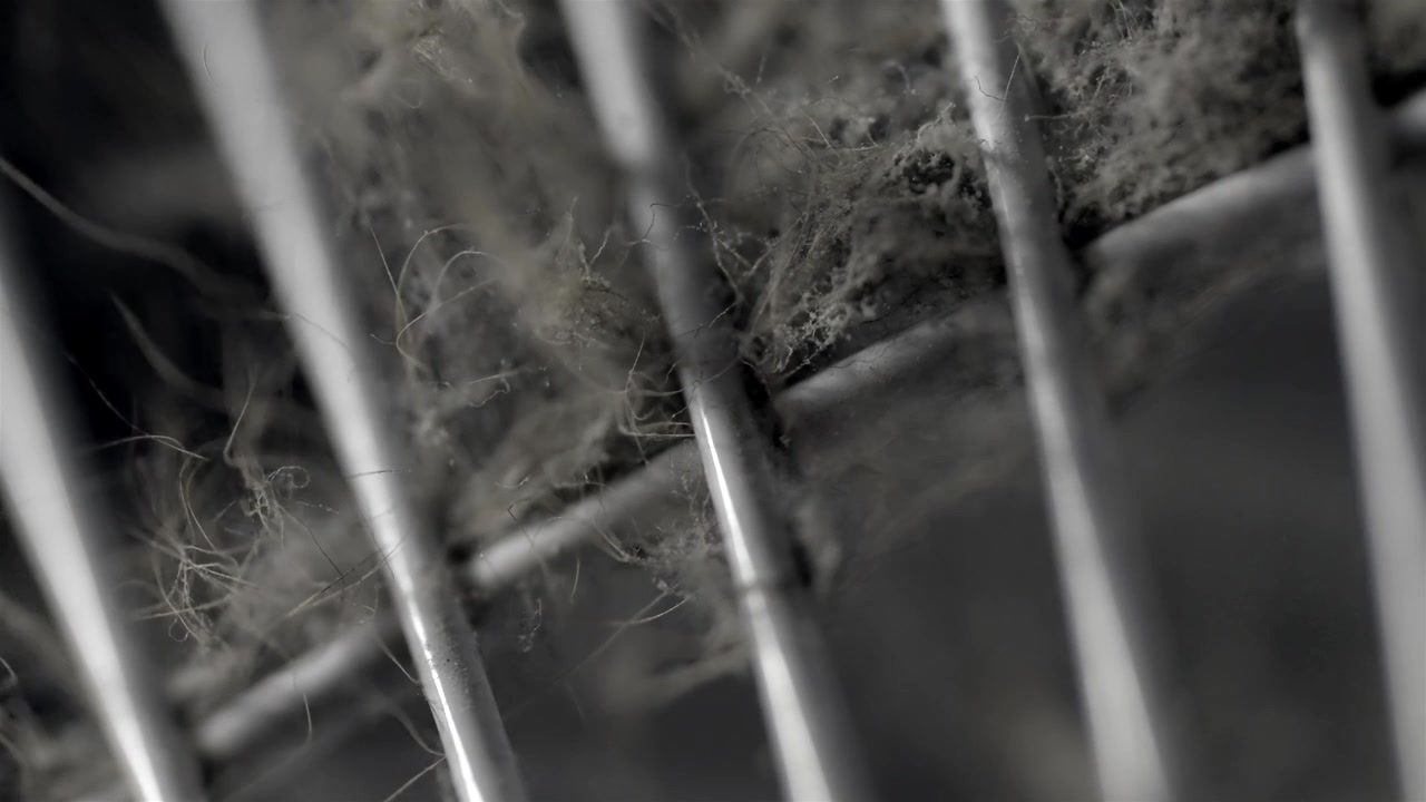 Dusty oscillating fan grille with metal bars fills a dark indoor close-up.