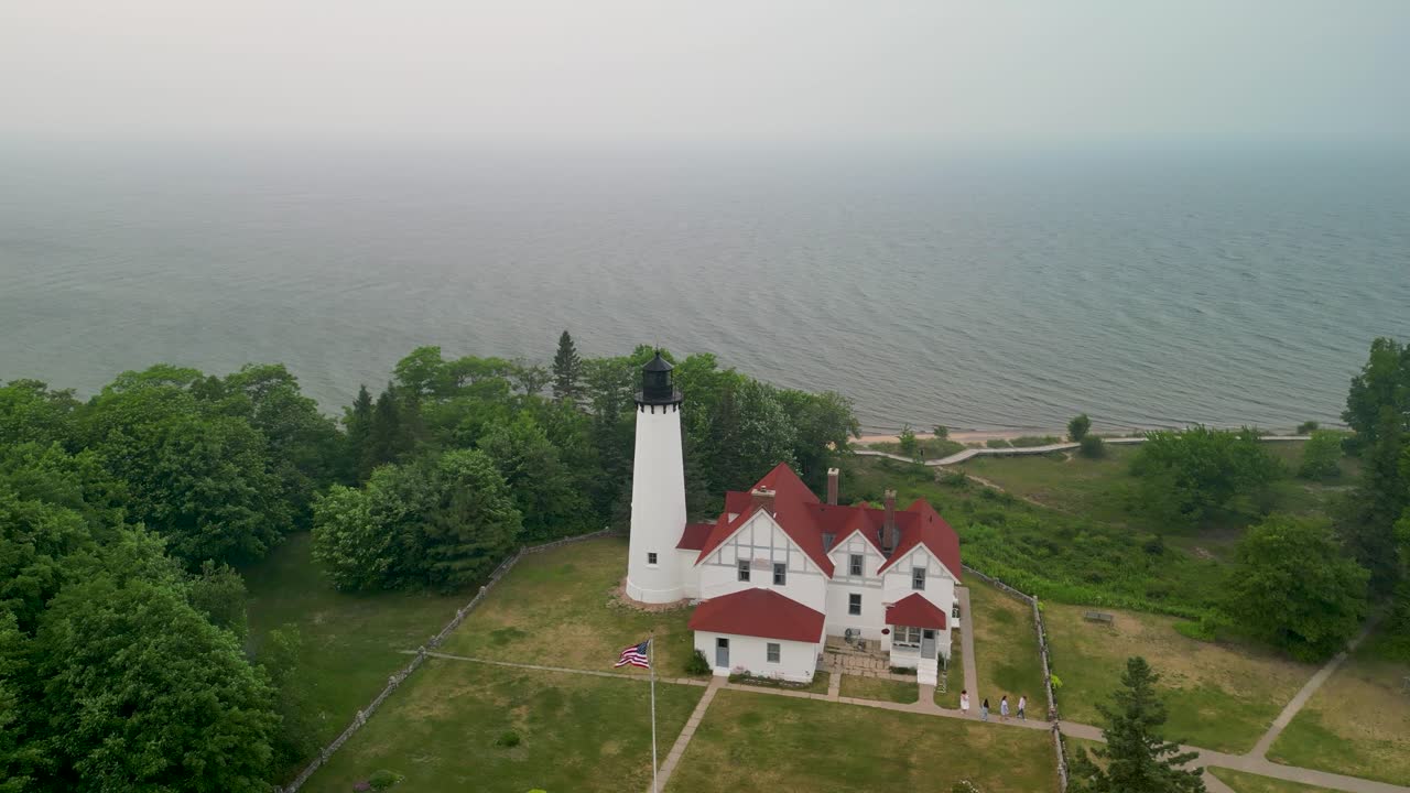 órbita aérea del faro de punto iriquois con humo de incendio forestal, lago superior, michigan