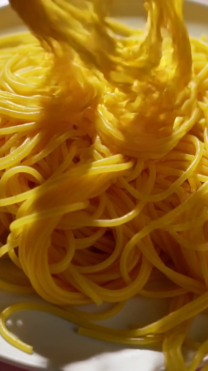 Vertical video: Dropping bundle of cooked yellow noodles forming dense pile on white plate to serve