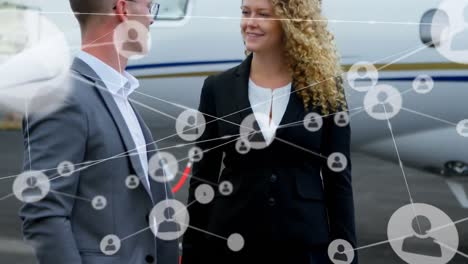 Animation-of-network-of-people-icons-over-caucasian-businessman-and-woman-talking-beside-airplane