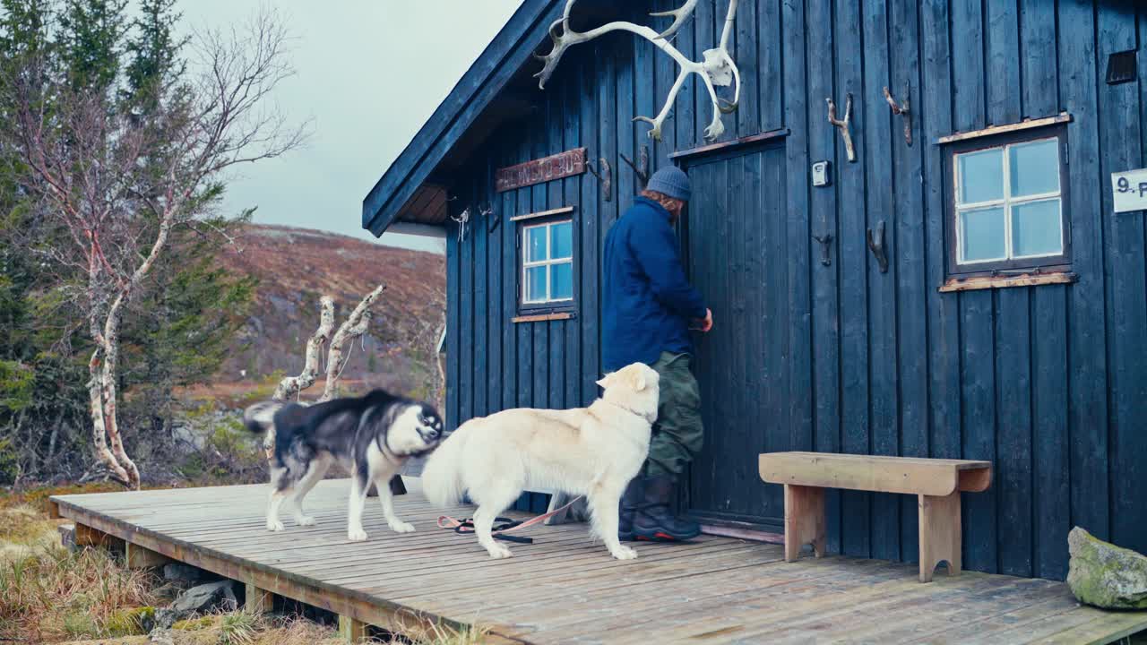 Man With His Dogs Sitting On The Cabin Porch. - wide shot
