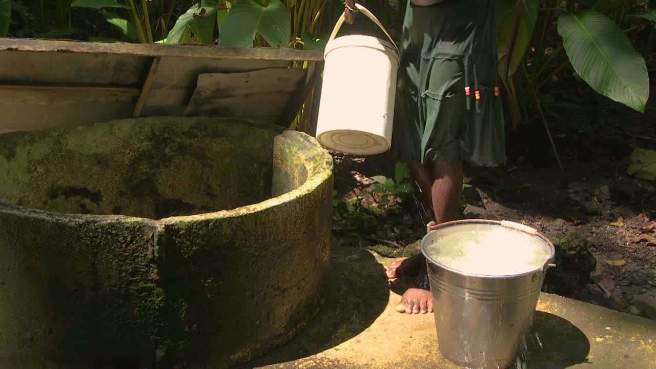 una niña que usa un balde para rellenar el agua de un pozo de agua