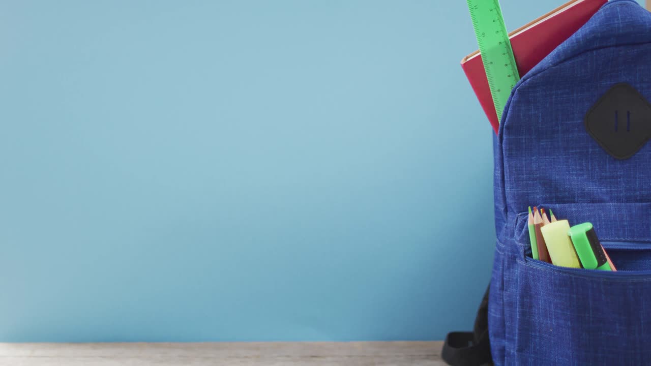 video de suministros escolares, cuaderno, bolígrafos, regla en la mochila sobre fondo azul