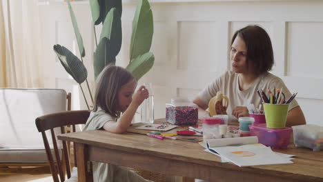 a happy mother holds a banana for her pretty blonde daughter as they play together with colored beads