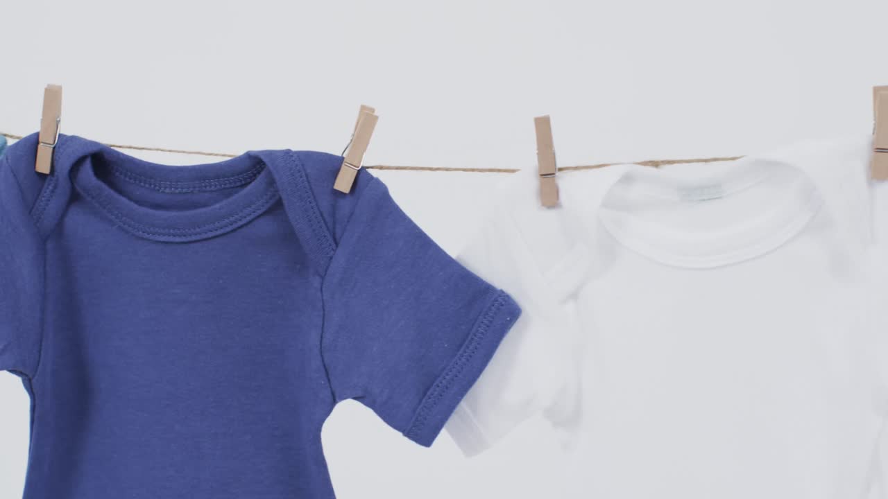 Video of multi coloured baby grows hanging on pegs from line with copy space on white background