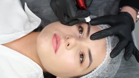 portrait of a girl microblading eyebrow tattoo permanent makeup the girl at the beautician portrait of a girl microblading eyebrow tattoo permanent makeup with the help of a special needle the master injects pigment into the skin and paints the eyebrows of a young girl