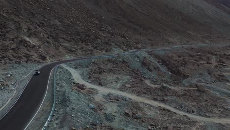 Aerial drone shot showing a car moving steadily across the rugged landscapes of Nubra Valley, with vast open spaces around.