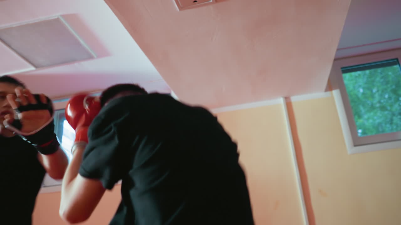 Grappler in black gloves and shirt raising guard during sparring session inside gym, showing combat readiness, discipline, focus, endurance, dynamic energy, power, martial determination