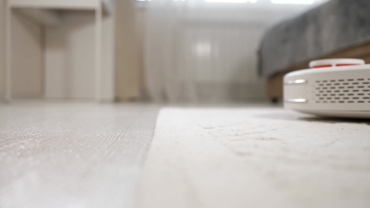 White robot vacuum cleaner hoovers floor driving to carpet