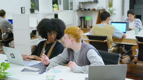 two young colleagues working together in open space office and discussing job