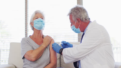 male caucasian doctor wearing face mask giving injection to senior caucasian woman at hospital