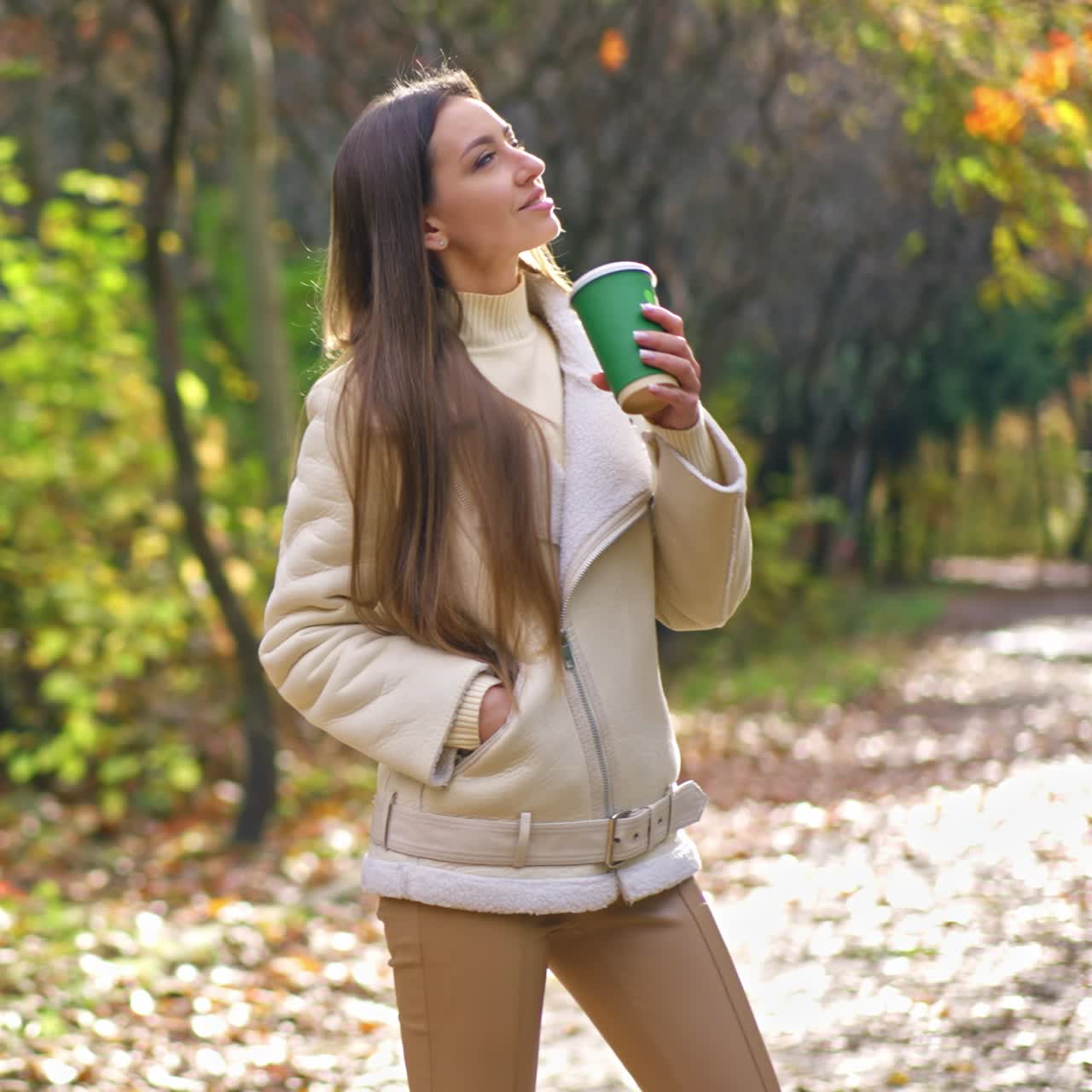 Signora dai capelli scuri con blazer color bianco latte che beve caffè al parco durante una passeggiata. Donna che passeggia da sola nella natura autunnale
