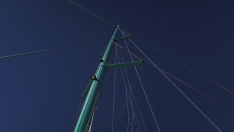 a shot from below the mast of a catamaran with the main sail lowered and many stringg going to the top