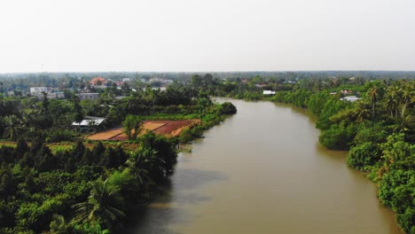 vista aérea de la región del delta del mekong en vietnam asia, vasto canal de agua marrón largo junto al río, ribera rodeada de aldea local, tierras agrícolas, vegetación y casas rurales