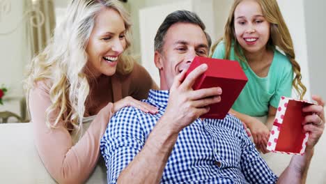 Padre-Abriendo-Caja-De-Regalo-Con-Esposa-E-Hija-En-La-Sala-De-Estar