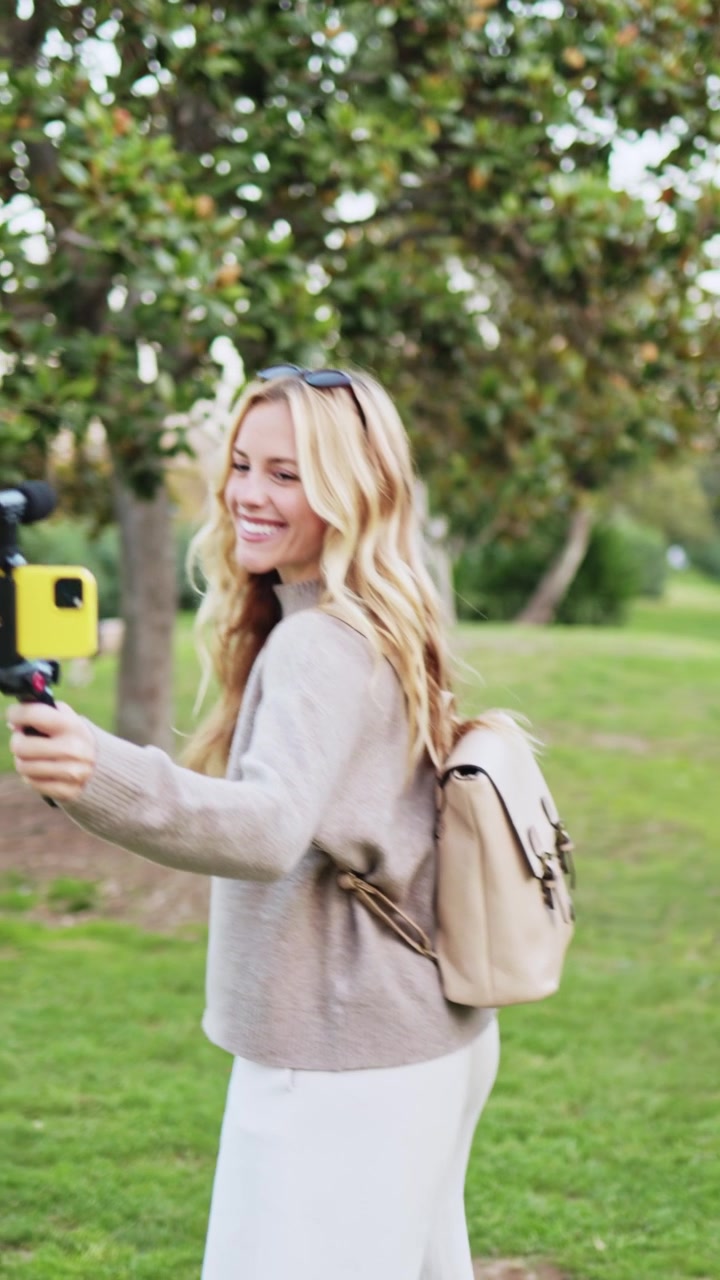Giovane donna felice che fa vlogging con smartphone e gimbal in un parco.