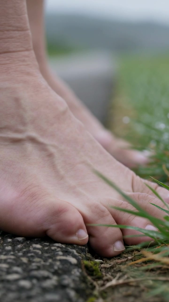 Vertical video: Feeling damp grass, barefoot adult pressing toes onto paved verge and curling