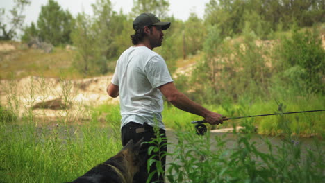 caucasian man accompanied by his german shepherd dog fly fishing in river