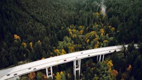 cinematic aerial reveal view of cars travelling through mountain highway bridge in fall, north vancouver bc