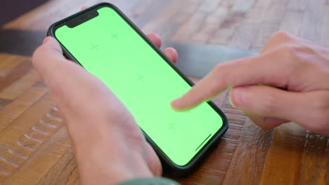 toma cinematográfica de una persona sosteniendo un iphone con una pantalla verde, tocando y deslizando la pantalla