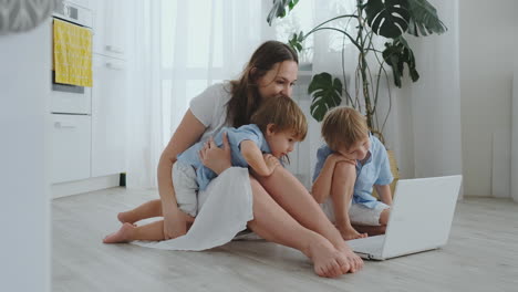 Apartamento-Moderno,-Mamá-Y-Dos-Hijos-Sentados-En-El-Suelo-De-La-Sala-De-Estar-Miran-La-Pantalla-Del-Portátil