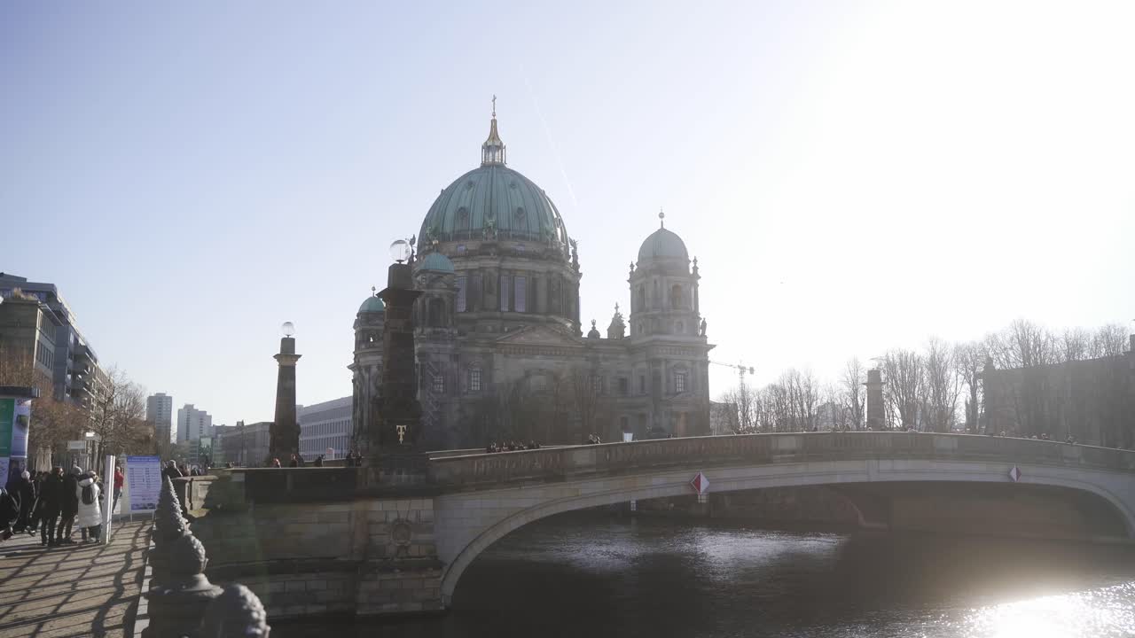 Et æstetisk skud af den historiske destination "Berliner Dom". I forgrunden ses en smuk, rolig flod. Turisterne går i centrum af Berlin i det skønne sommervejr
