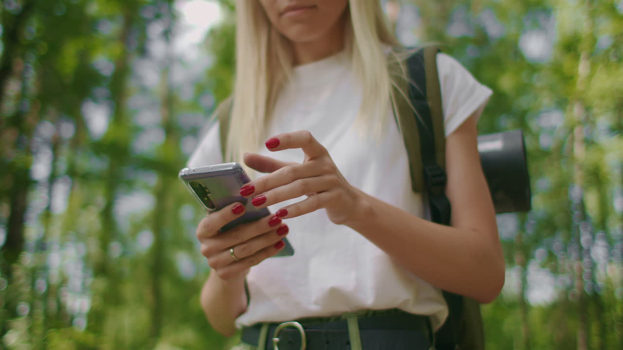 Close-up of a mobile phone in the hands of a female traveler walking through the forest. Social networks Navigator and messenger. Use your mobile phone for a walk in the woods