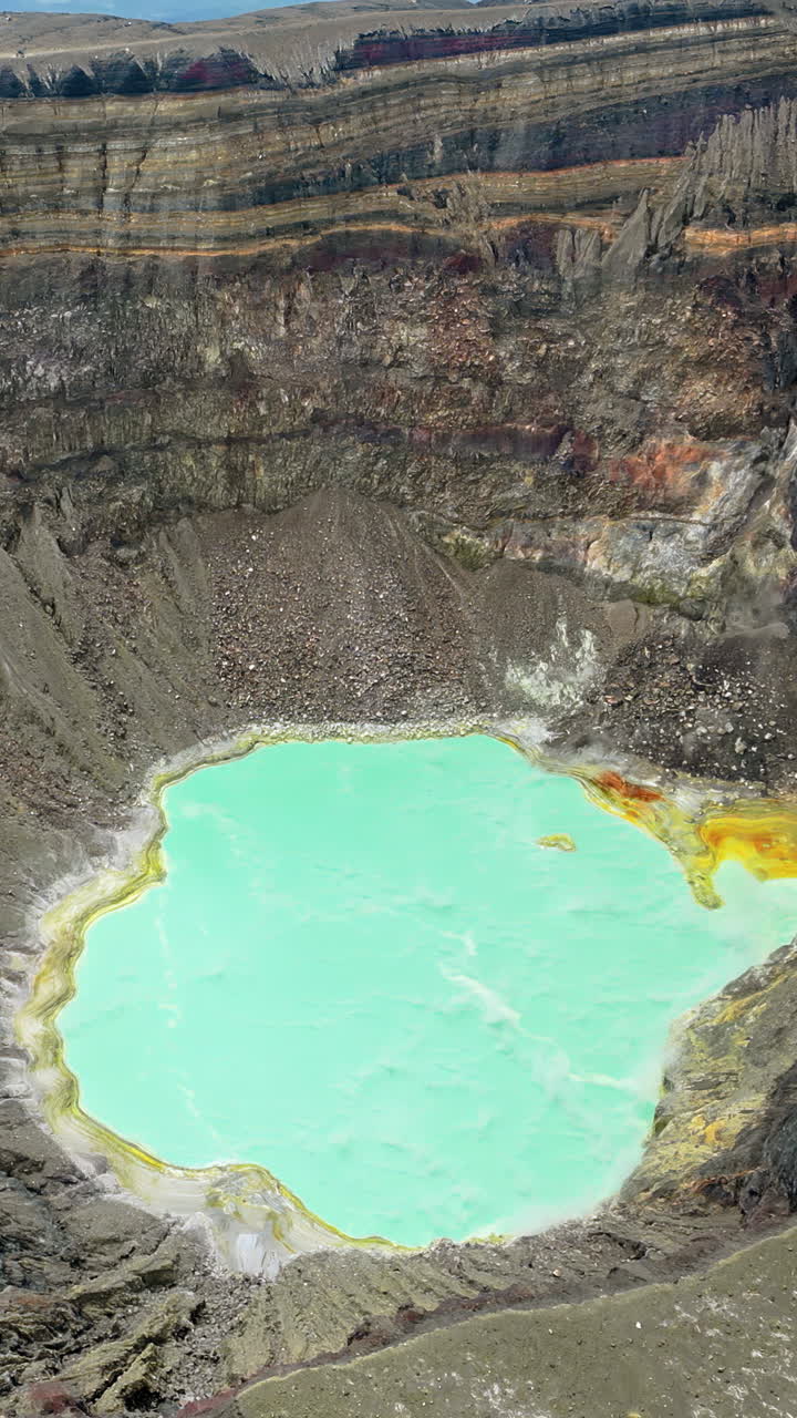 Aerial drone view of a turquoise crater lake inside a volcanic crater in Guatemala, surrounded by rugged volcanic rock formations and geothermal landscape. Vertical