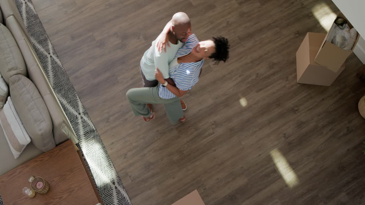 African American couple hugging and turning on living room floor after moving boxes, celebrating