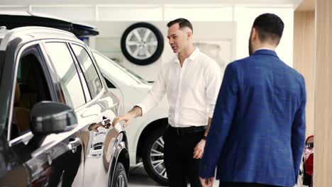 un cliente masculino eligiendo un coche en el concesionario con la ayuda de un vendedor de automóviles, cámara lenta