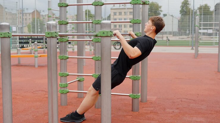 Young european man performing an inverted row bodyweight exercise on an outdoor calisthenics gym, training upper body strength and fitness for a healthy lifestyle, static camera, slow motion