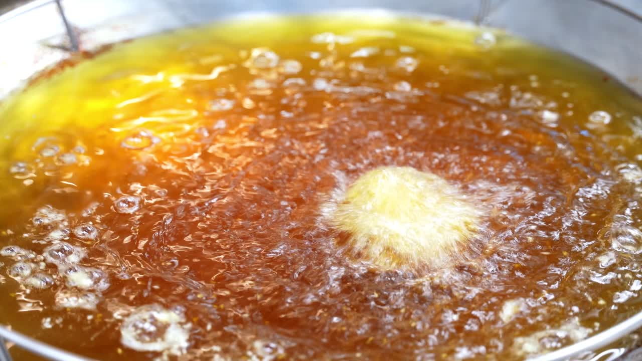 Close-up shot of gloved hand frying food in hot bubbling oil, perfect for cooking, street food, and culinary process videos for food marketing or tutorials