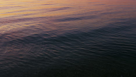 Nahaufnahme-Der-Ruhigen-Wasseroberfläche-Des-Ozeans,-Die-Am-Morgen-Den-Leuchtend-Rosafarbenen-Sonnenaufgangshimmel-Reflektiert