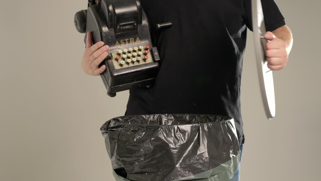 한 남자가 오래된 현금 계산기를 쓰레기통에 던지고 있다.