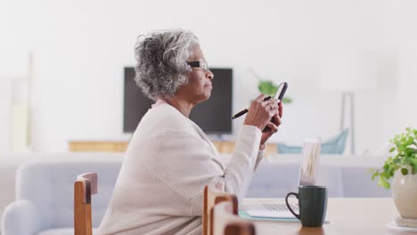 Portrait-of-happy-senior-african-american-woman-sitting-at-table,-using-smartphone