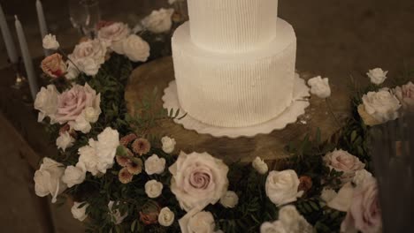 close-up of a wedding cake surrounded by roses and greenery on a rustic table