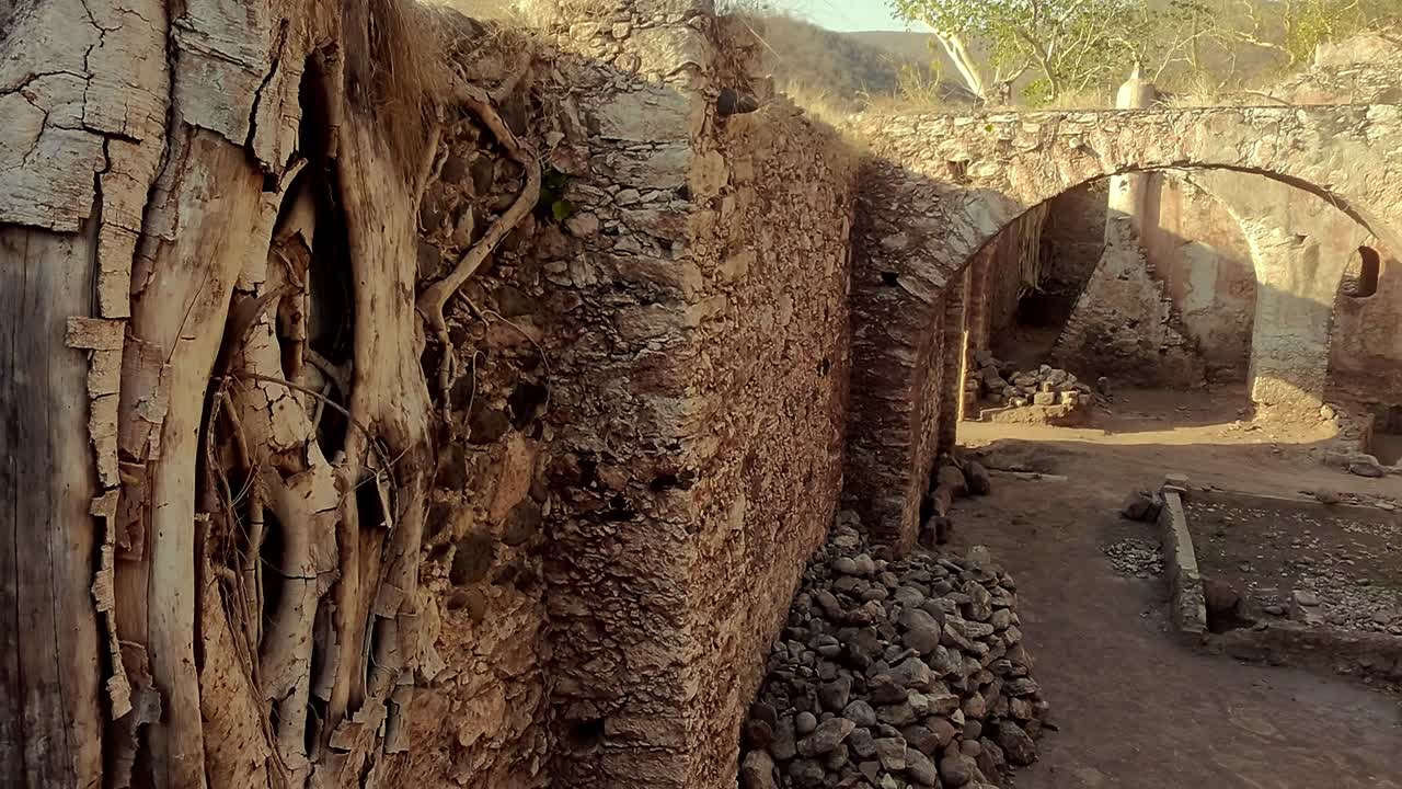 Old stone walls with tree roots, sunlight and ruins of Hacienda Ixtoluca in view