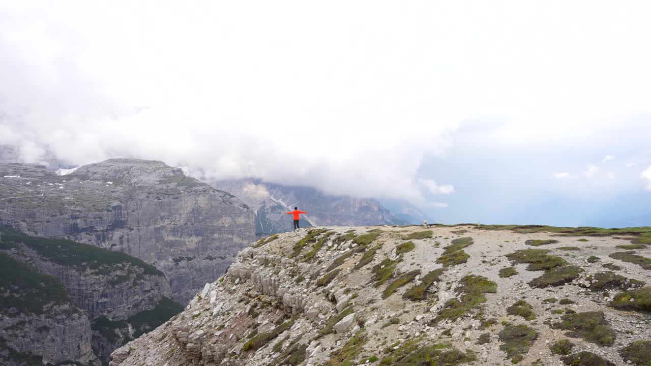 hombre con chaqueta corre al borde del acantilado brazos extendidos admirando la belleza del valle de auronzo