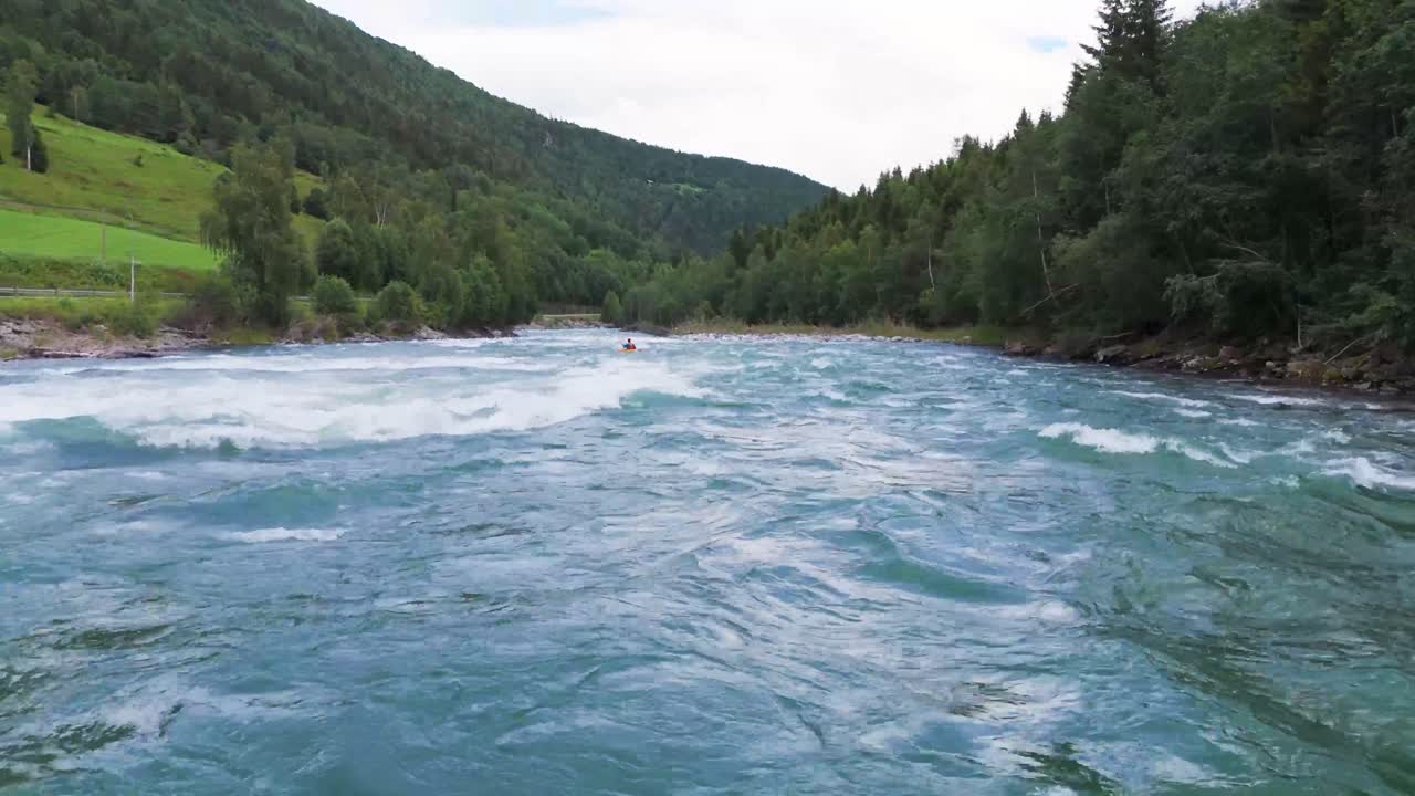 Aerial view of a kayaker navigating white water rapids through a picturesque river surrounded by lush greenery and mountains
